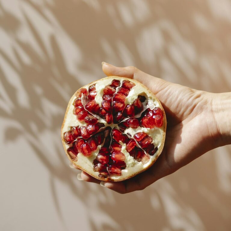 Pomegranate half held against warm shadows, showcasing fresh seeds.